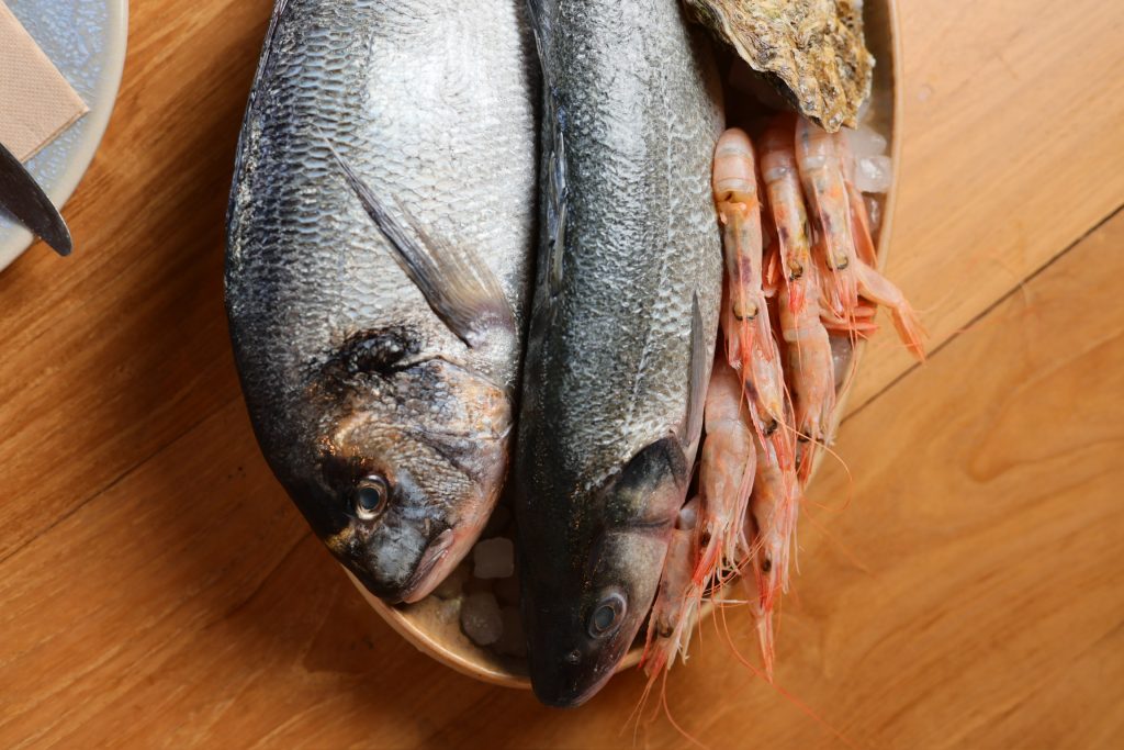 Pescado fresco entero y gambas sobre tabla de madera.